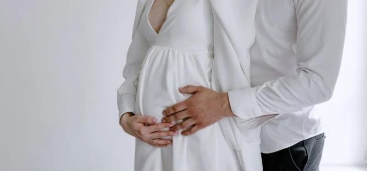 Expectant father and mother in white attire holding hands
