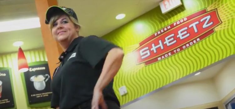 Woman in black shirt and hat standing in front of Sheetz logo to help customers